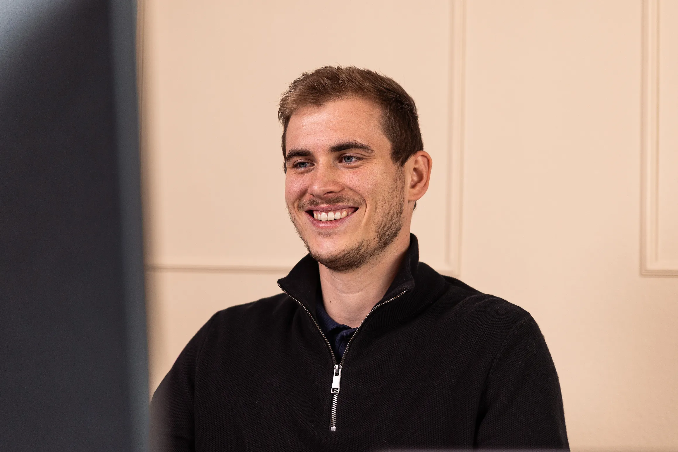 Lächelnder Mann mit kurzem braunem Haar schaut auf einen Bildschirm vor sich.