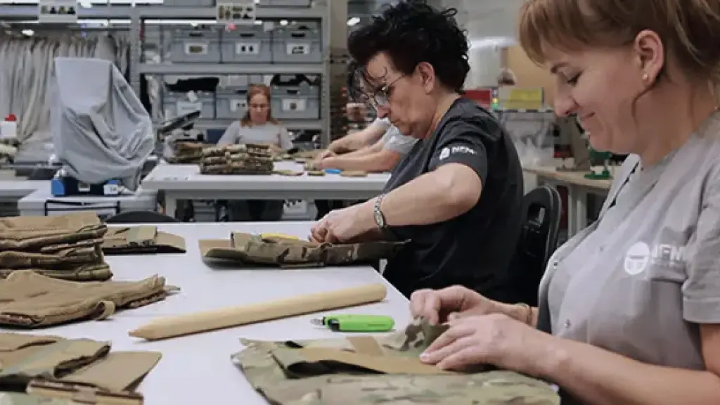 Four women working at tables assembling or inspecting folded brown fabric pieces in a workshop setting.