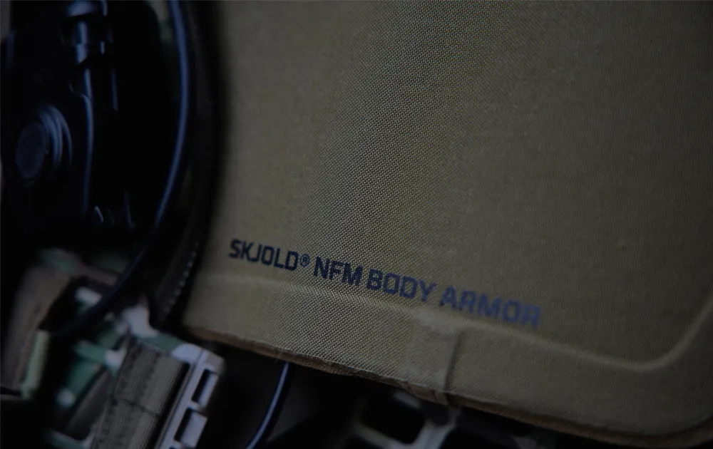 Close-up of olive green SKJOLD® NFM body armor with visible text logo.