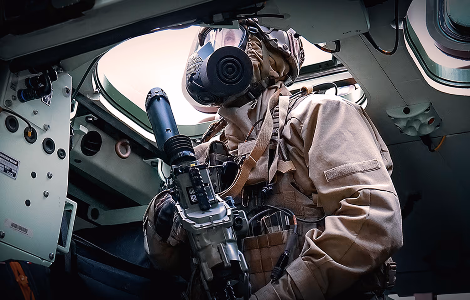 Soldier in tactical gear wearing a gas mask and helmet holding a weapon inside an armored vehicle.