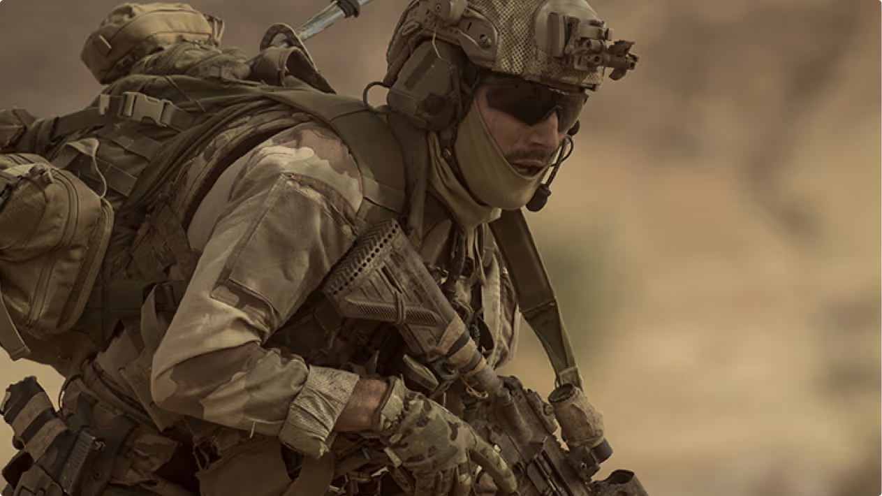 Soldier wearing tactical gear and helmet, holding a rifle in a desert environment.