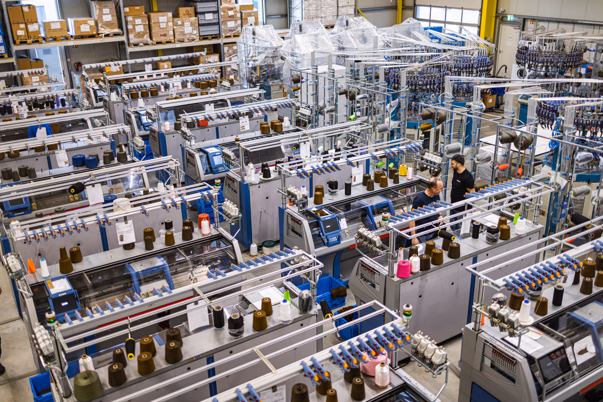 Industrial textile factory with multiple knitting machines and workers operating them.