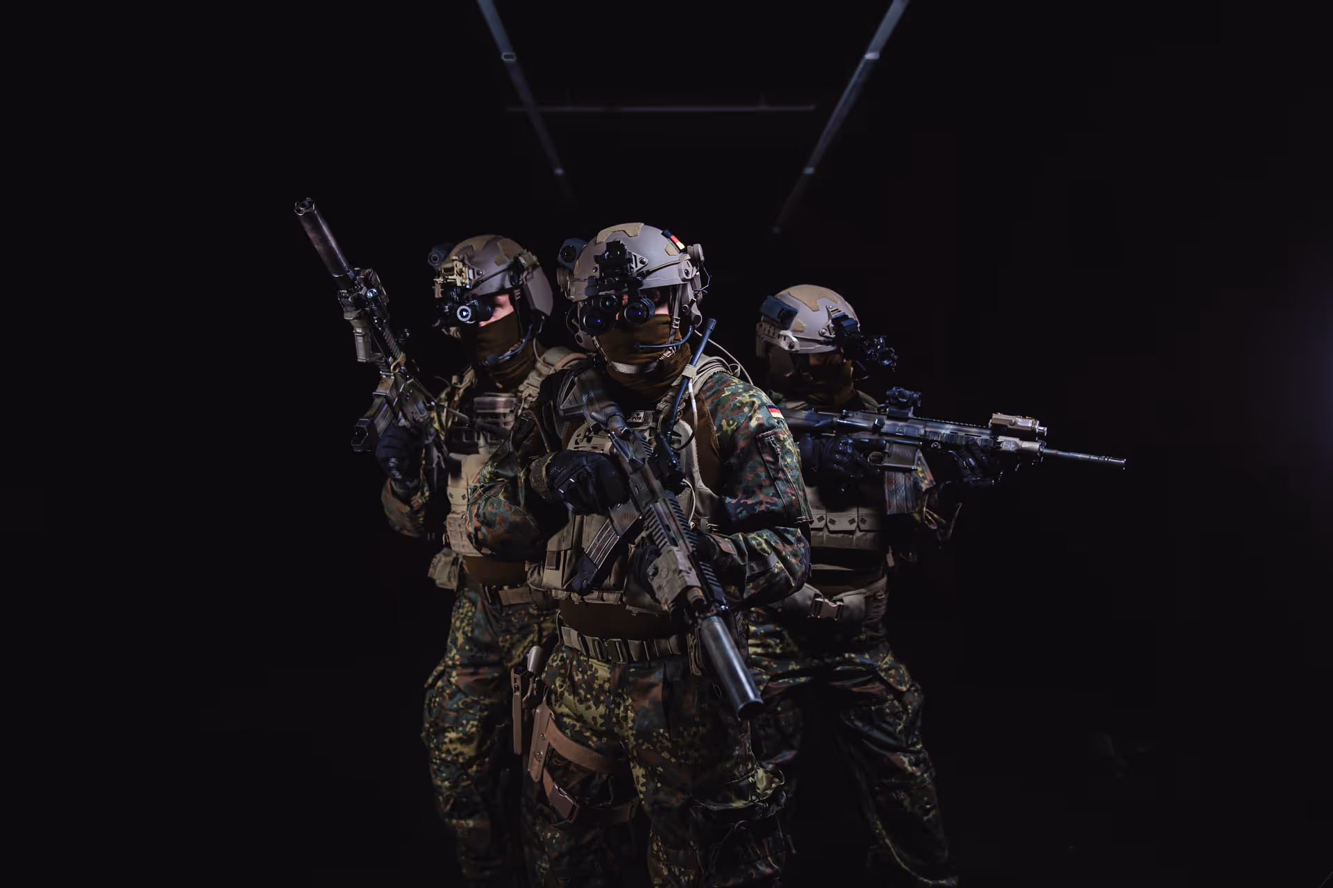 Three soldiers in camouflage uniforms and tactical gear aiming rifles in a dark setting.