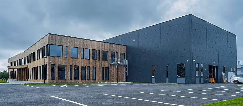 Modern commercial building with wood-paneled facade and large black warehouse section under a cloudy sky.