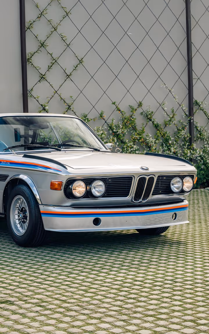Classic BMW 3.0 CSL with racing stripes on brick pavement.