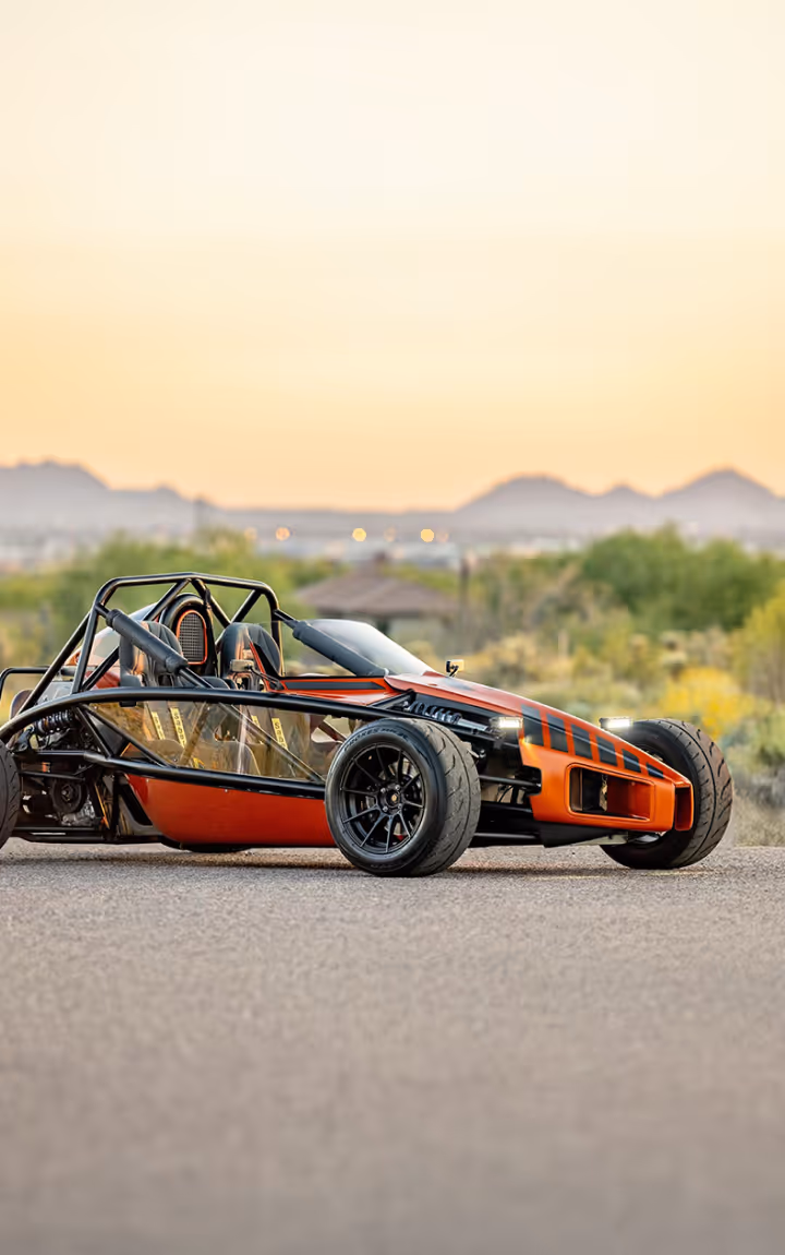 Orange and black race car on desert road at sunset.