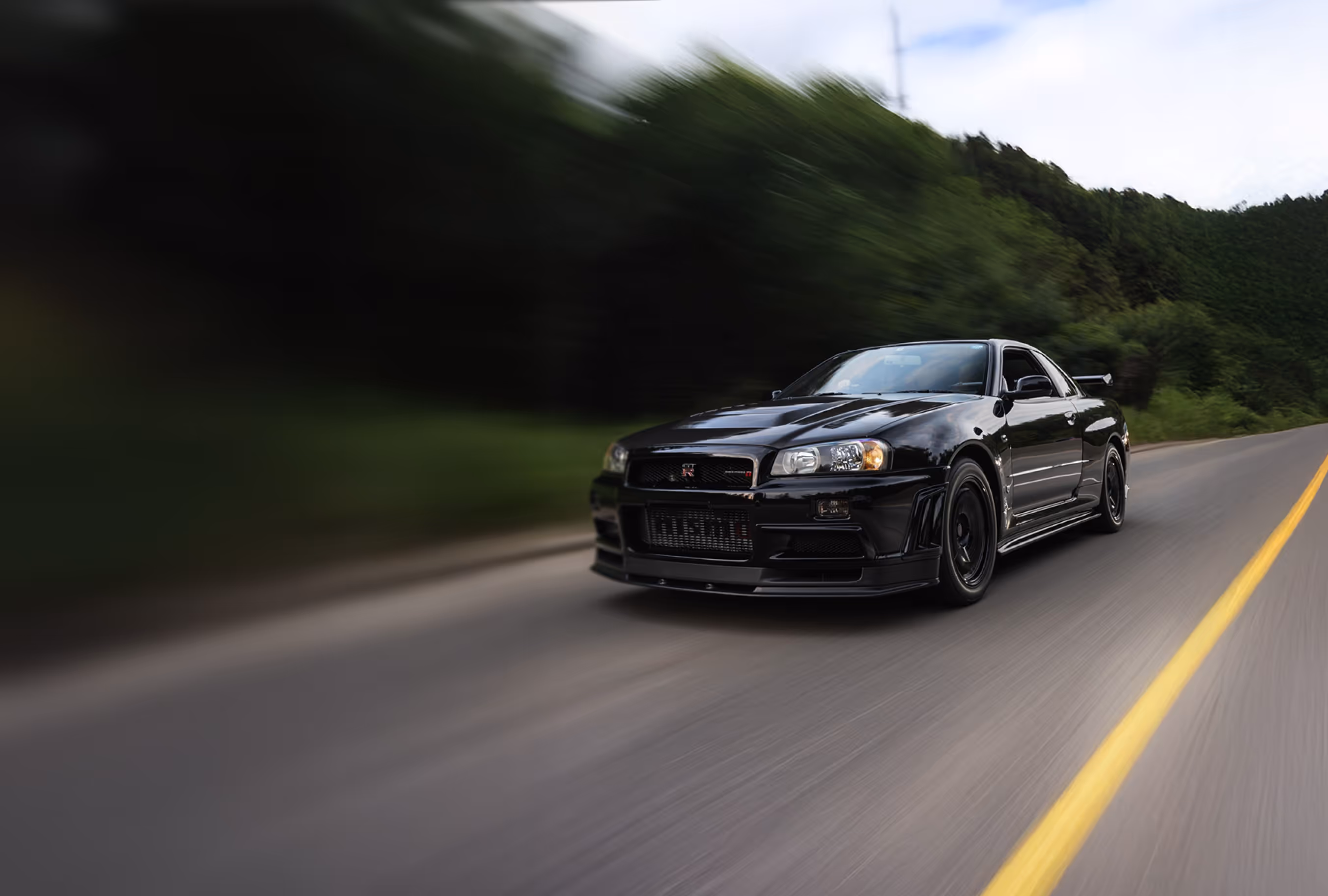 Black Nissan Skyline GT-R driving on forest road.