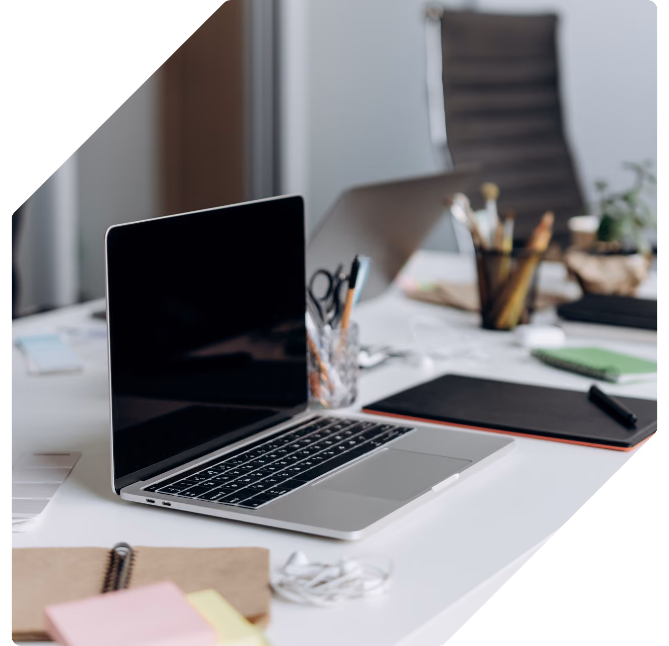 An open laptop on a bright desk with a graphics tablet, notebook and pens arranged around it.