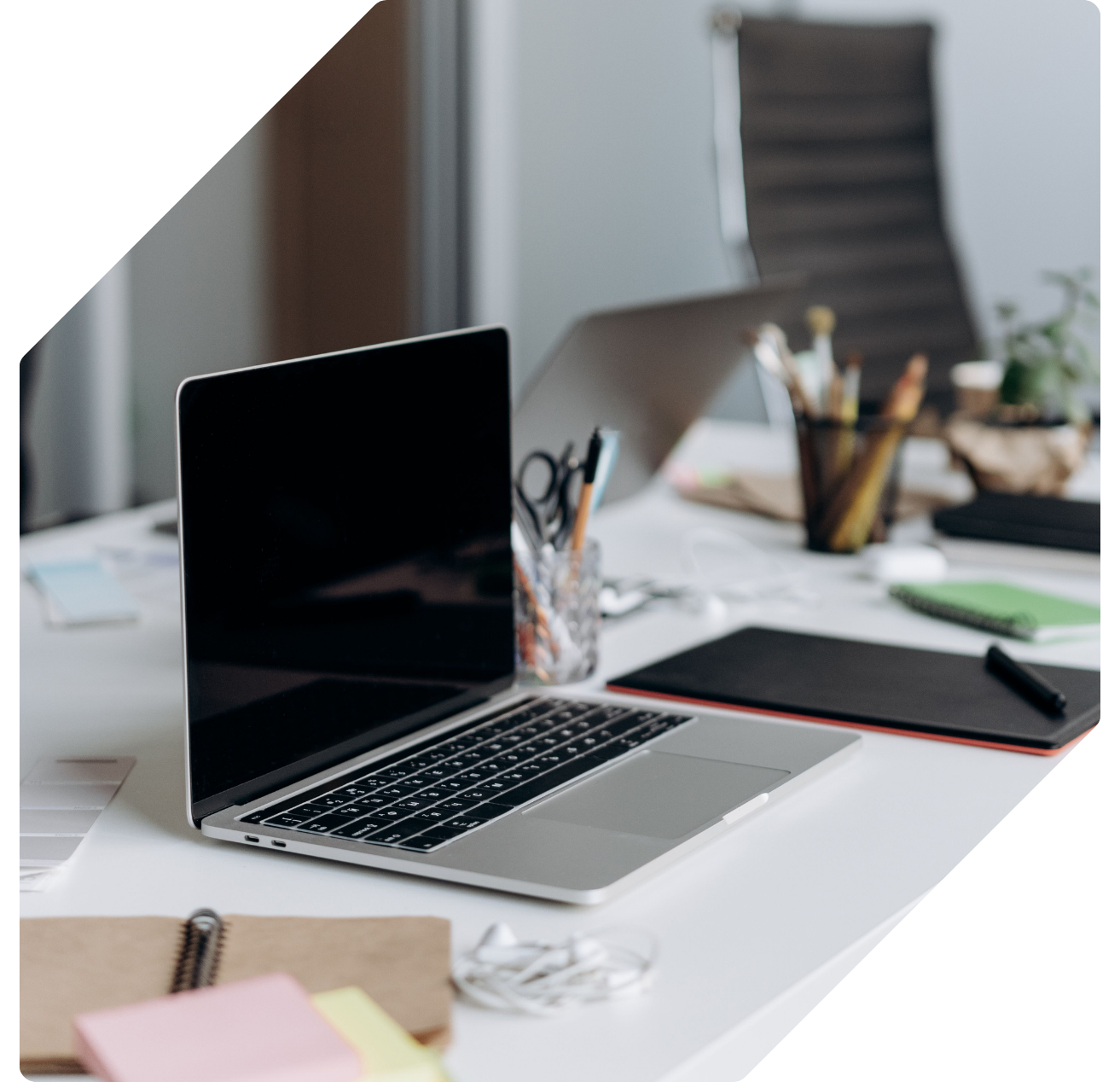 An open laptop on a bright desk with a graphics tablet, notebook and pens arranged around it.
