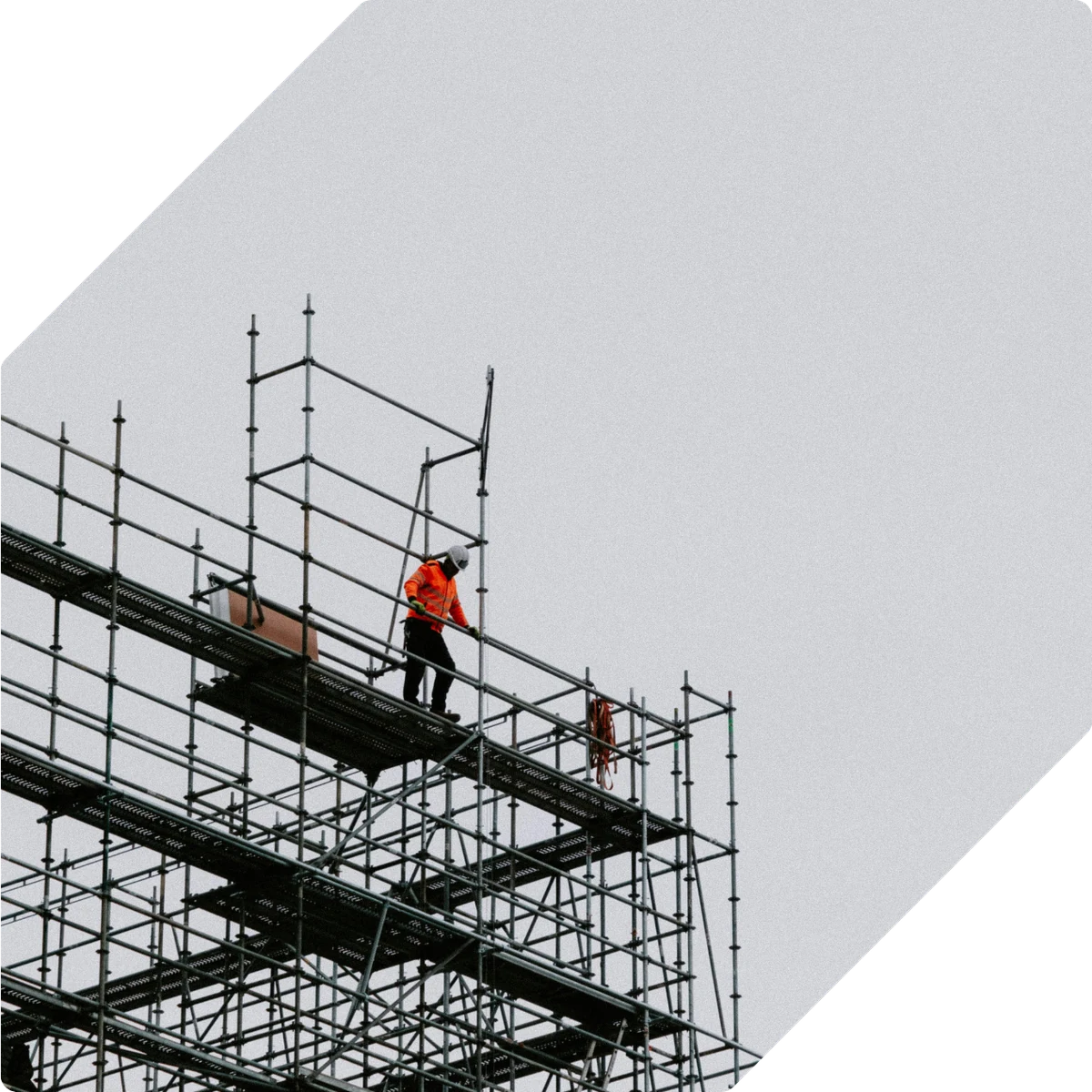 A worker in a high-visibility jacket on the upper deck of scaffolding around a building under construction.