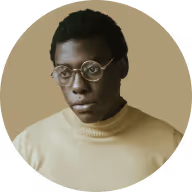 Portrait of a man with glasses wearing a light brown turtleneck against a beige background.