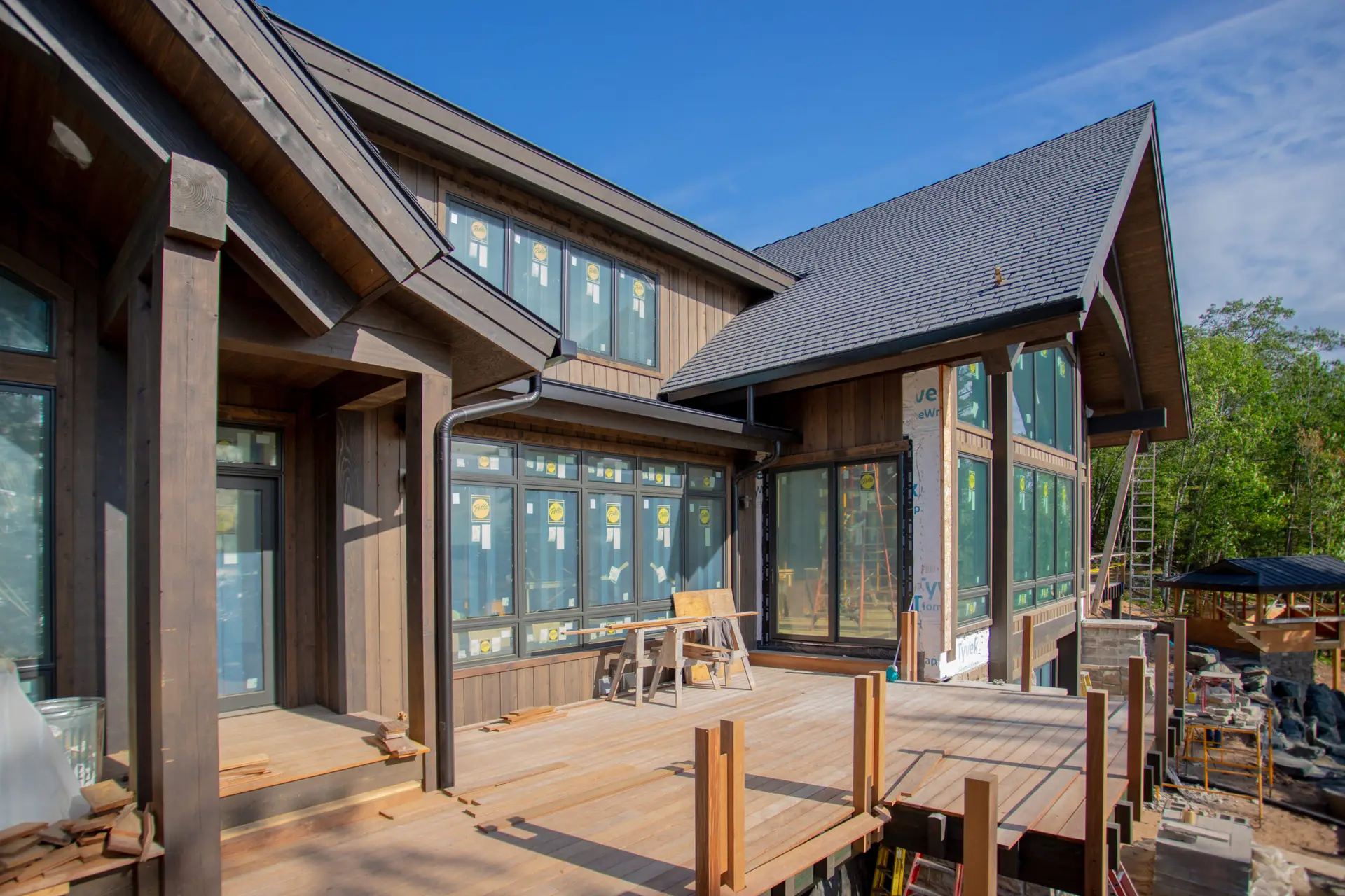 Modern wooden house under construction with large windows and a spacious wooden deck.