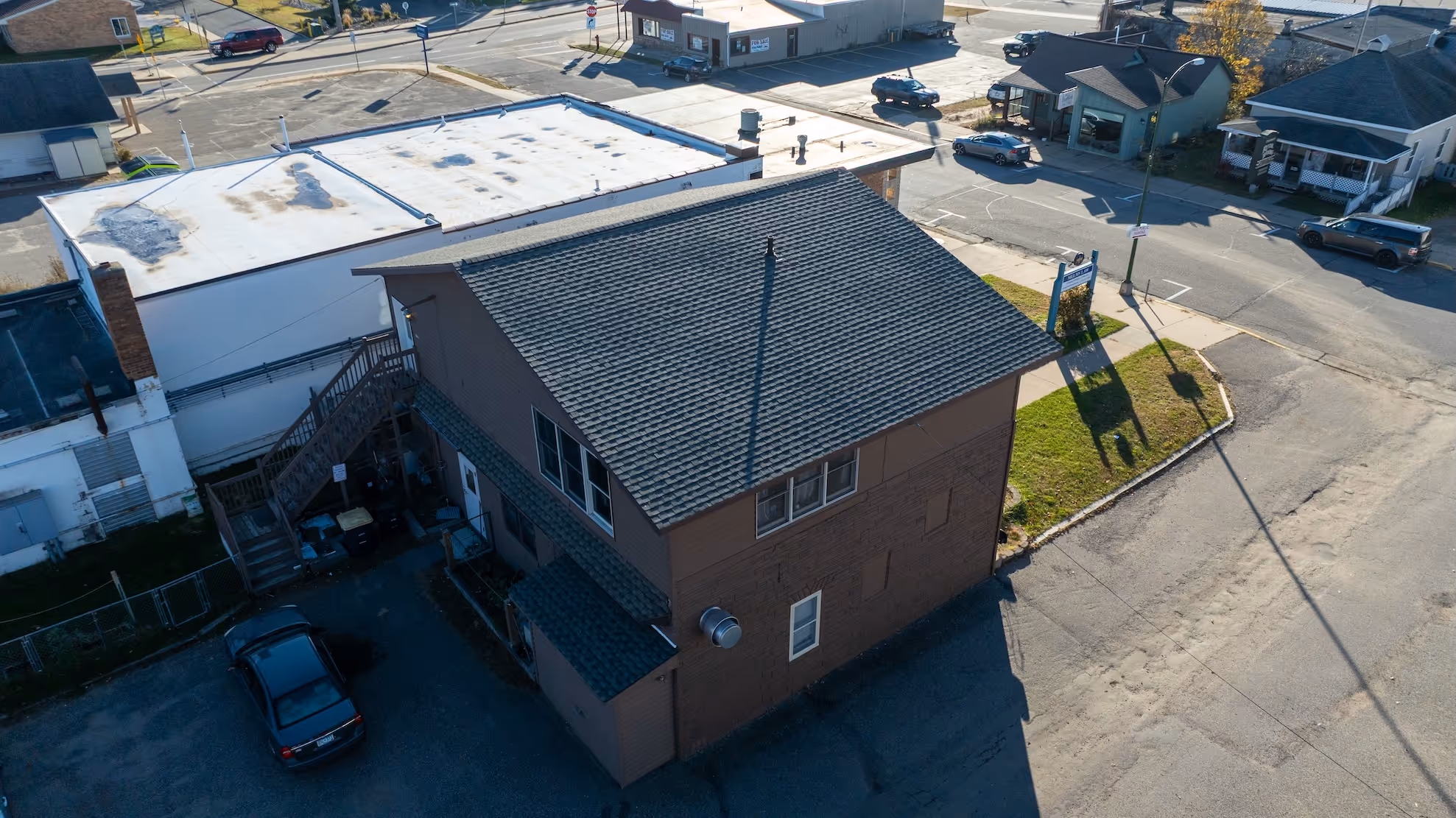 Aerial view of a two-story brown building with a shingled roof, surrounded by streets and parked cars.