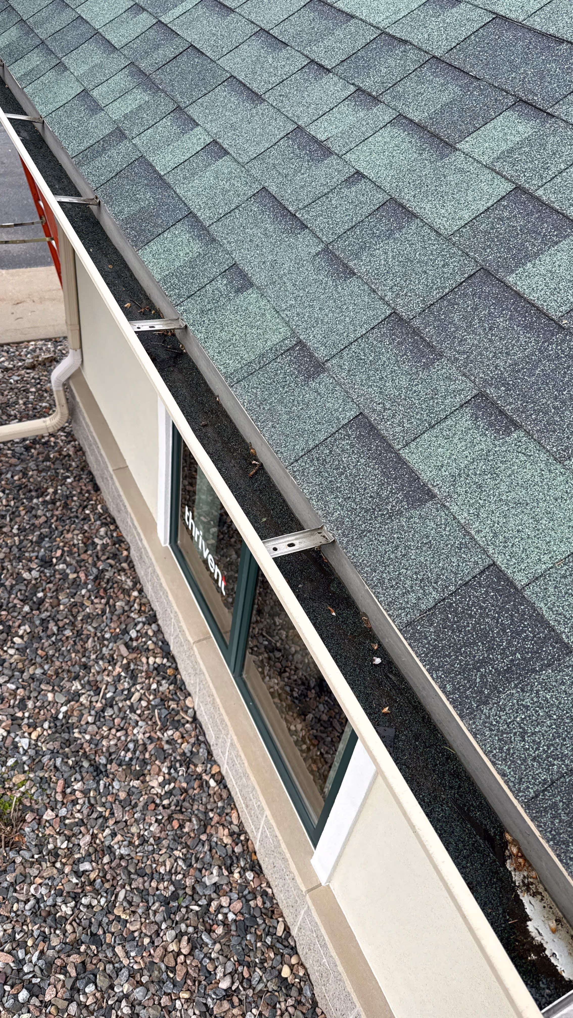 Close-up view of a house roof with green asphalt shingles and a gutter filled with debris.
