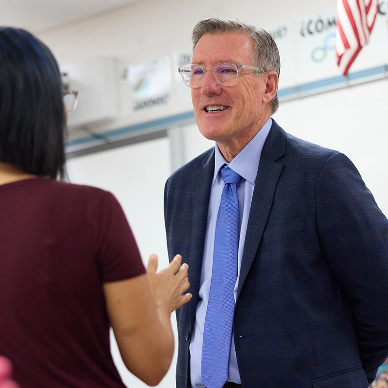 Kelly talking to a woman wearing glasses and a maroon top in a classroom setting.