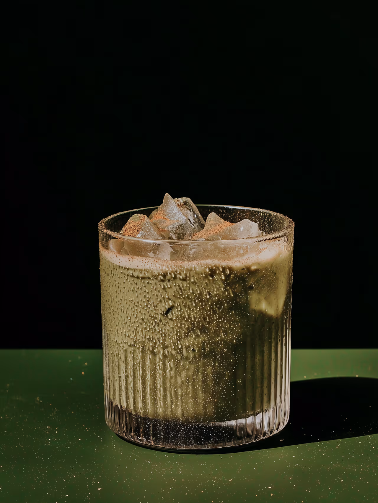 Iced matcha latte with vibrant green layers in a glass, with ice cubes.