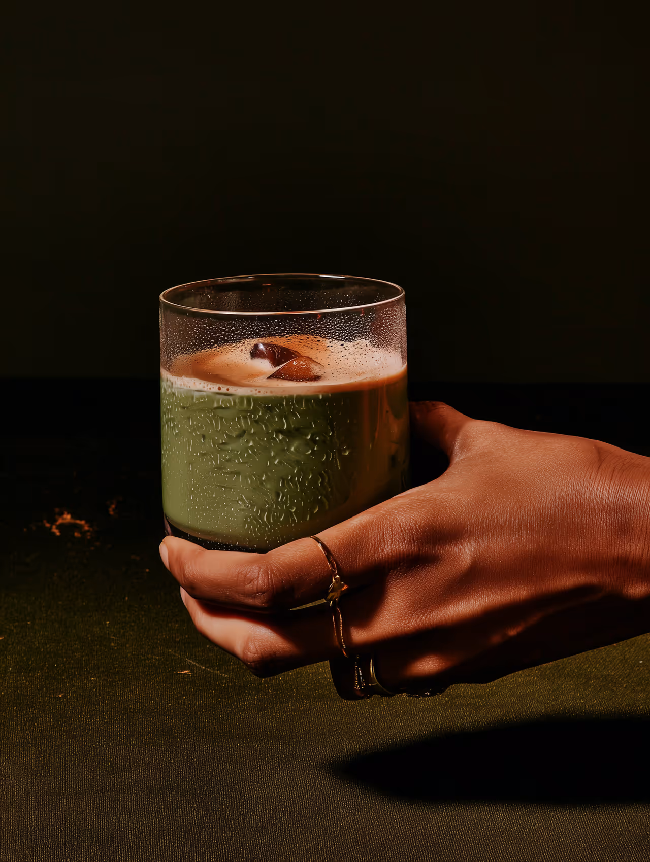 A hand is holding a frothy green matcha latte in an elegant glass.