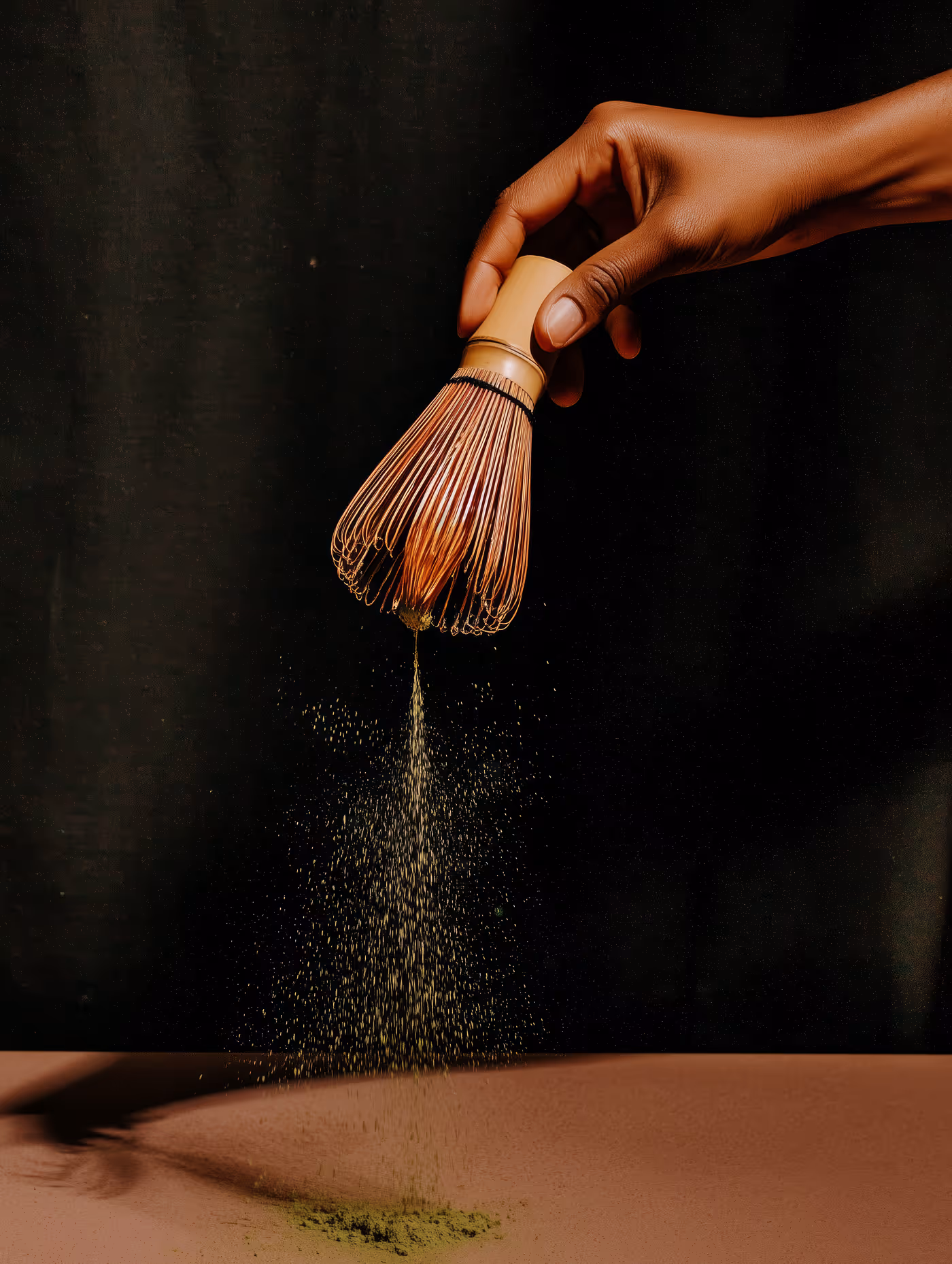 Hand is holding a ceremonial matcha whisk pouring matcha tea on a table.