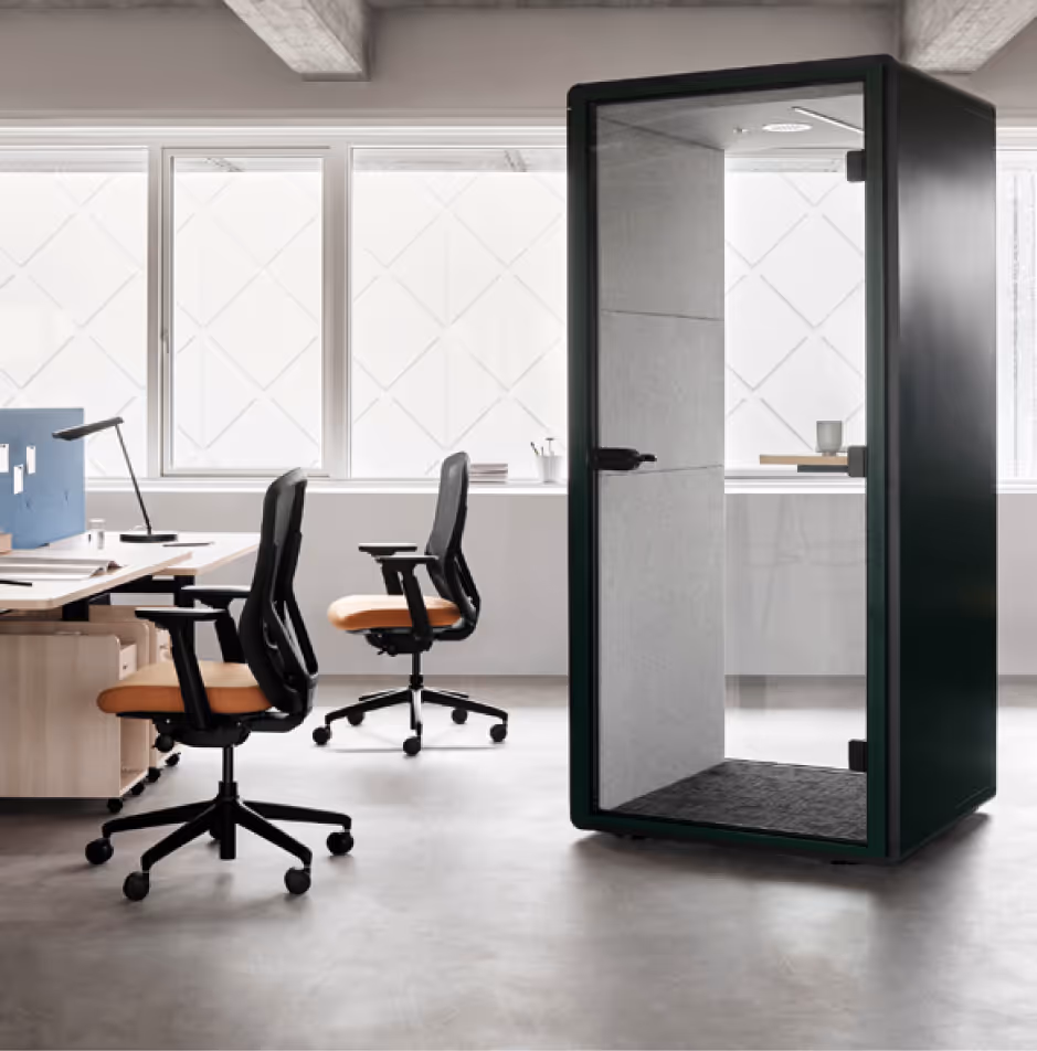 Modern office space with two ergonomic chairs at desks and a black soundproof phone booth with glass door.
