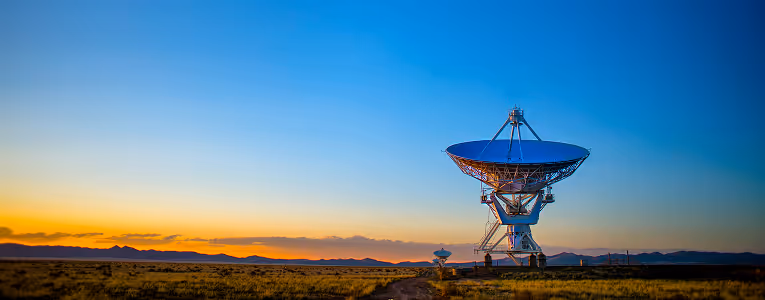 Large radio telescope dish in a desert at sunset with mountains in the background.