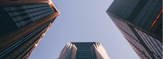 Upward view of three tall modern skyscrapers against a clear blue sky.