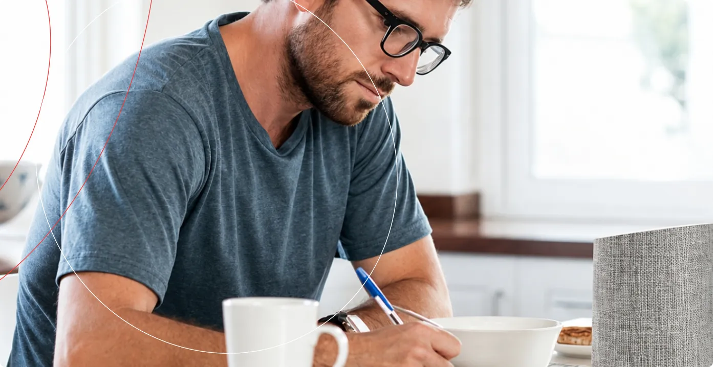 Man in glasses writing notes at a desk in a bright room