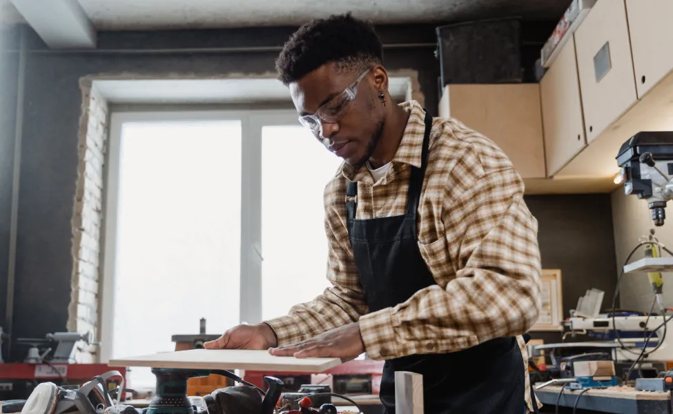 Craftsman in safety glasses shaping a wooden panel in a workshop