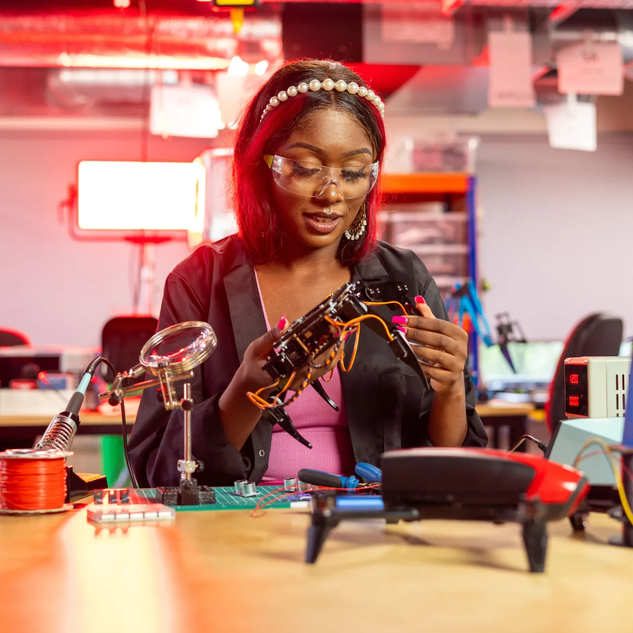 Young engineer in safety glasses assembling a robotic part at an electronics workbench
