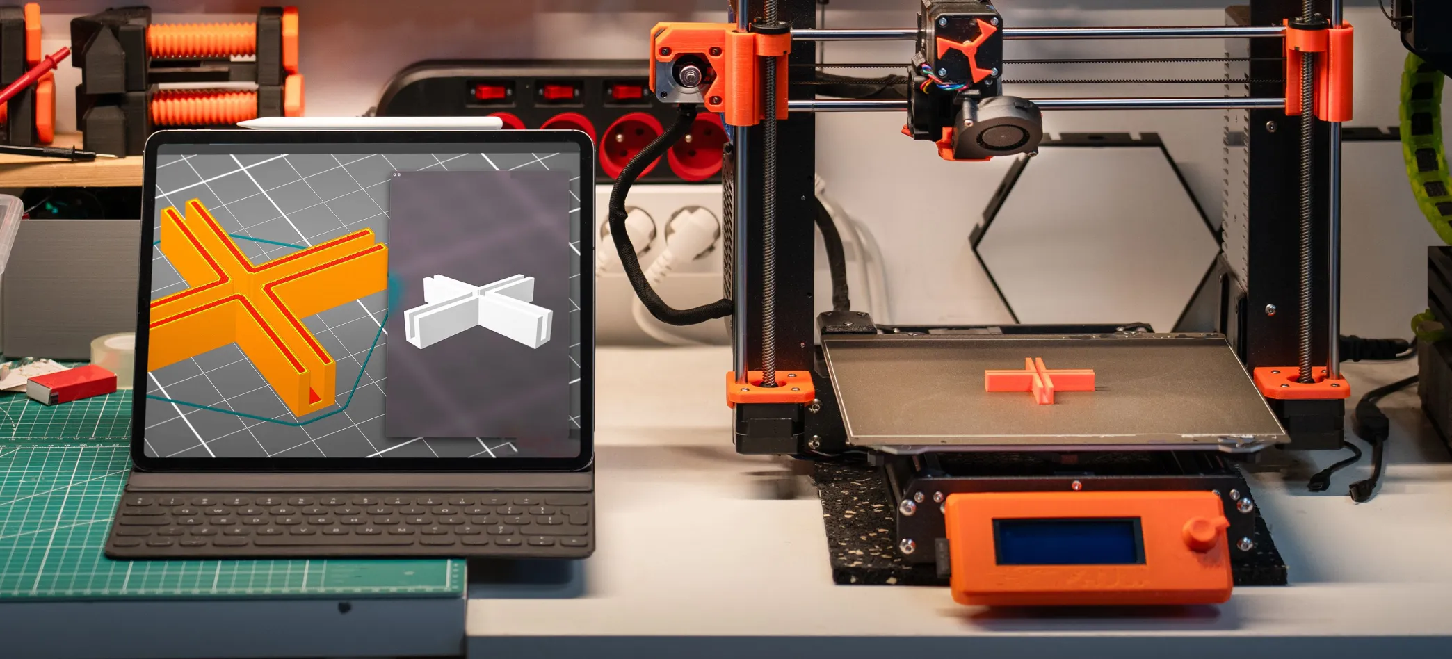 3D printer producing a part next to a tablet showing its 3D model