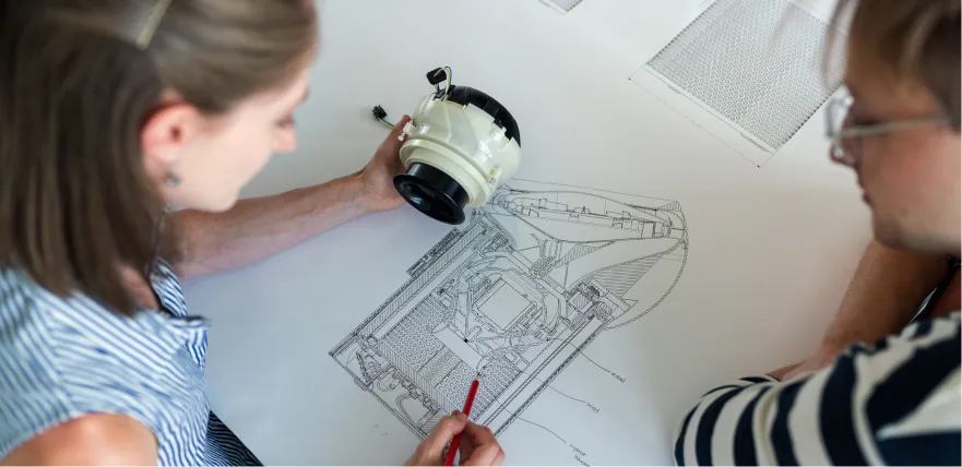 Two engineers reviewing a pump assembly against its technical drawing