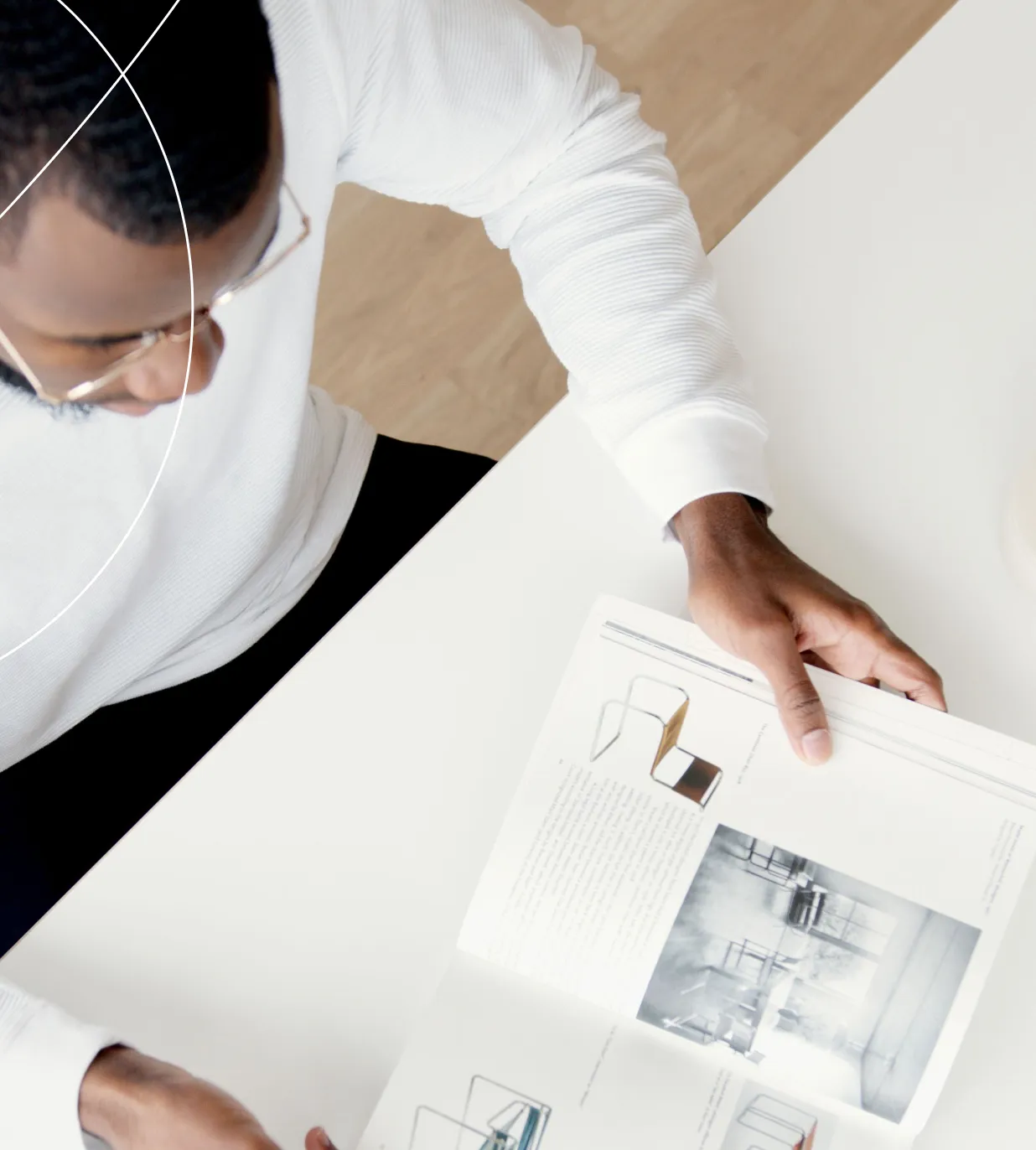 Designer at a white desk turning the page of a product design book filled with furniture sketches