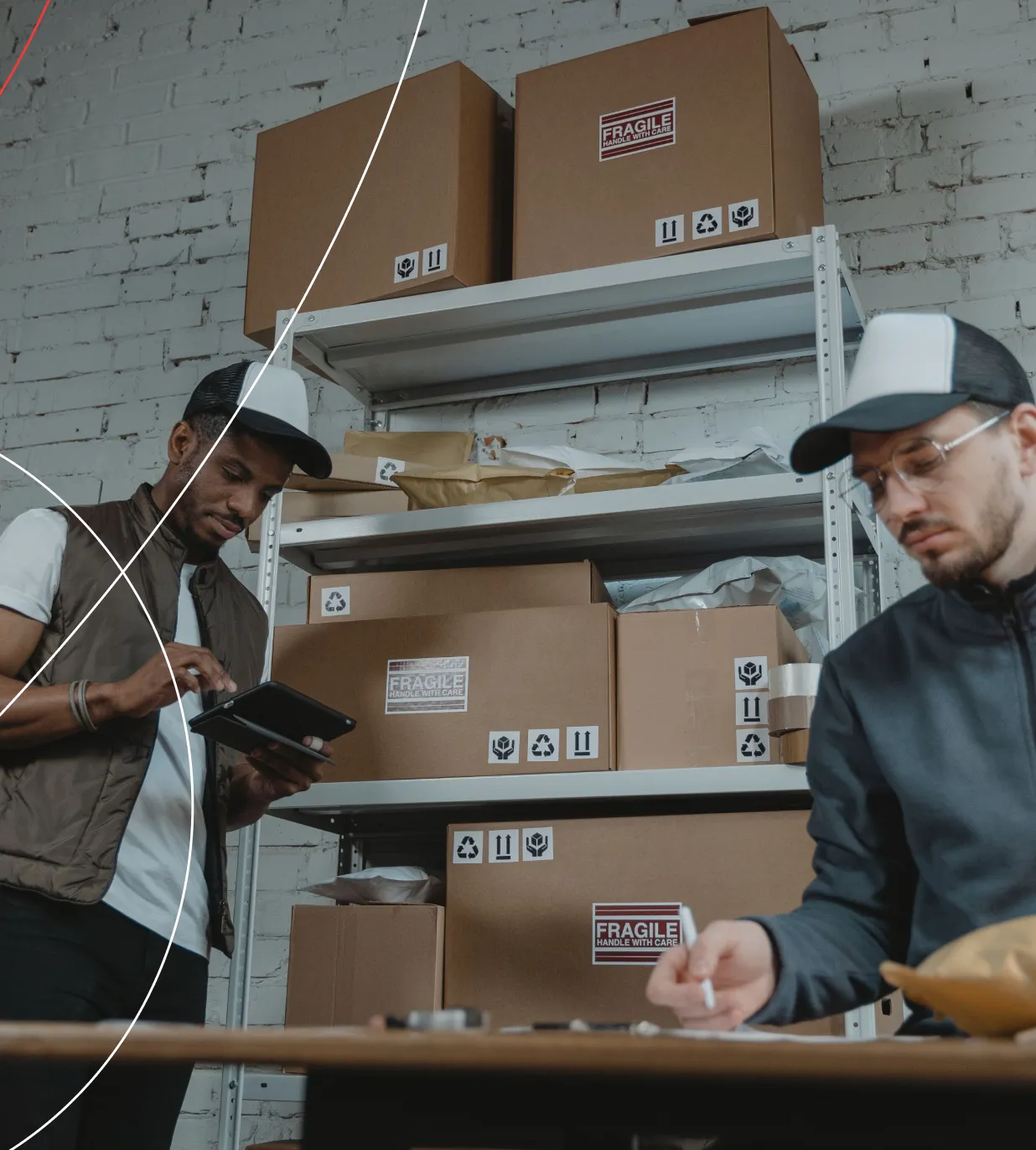 Two people in a stockroom checking packed cartons, one logging items on a tablet and the other labelling a box