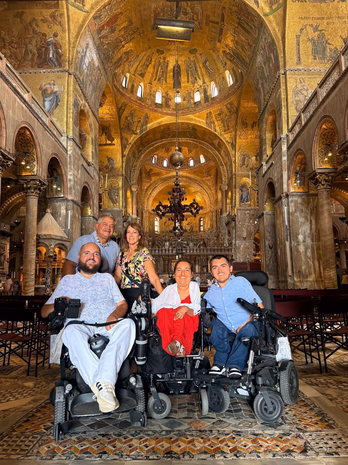 A family, including three people in power wheelchairs, inside the Basilica di San Marco. They are surrounded by gold.