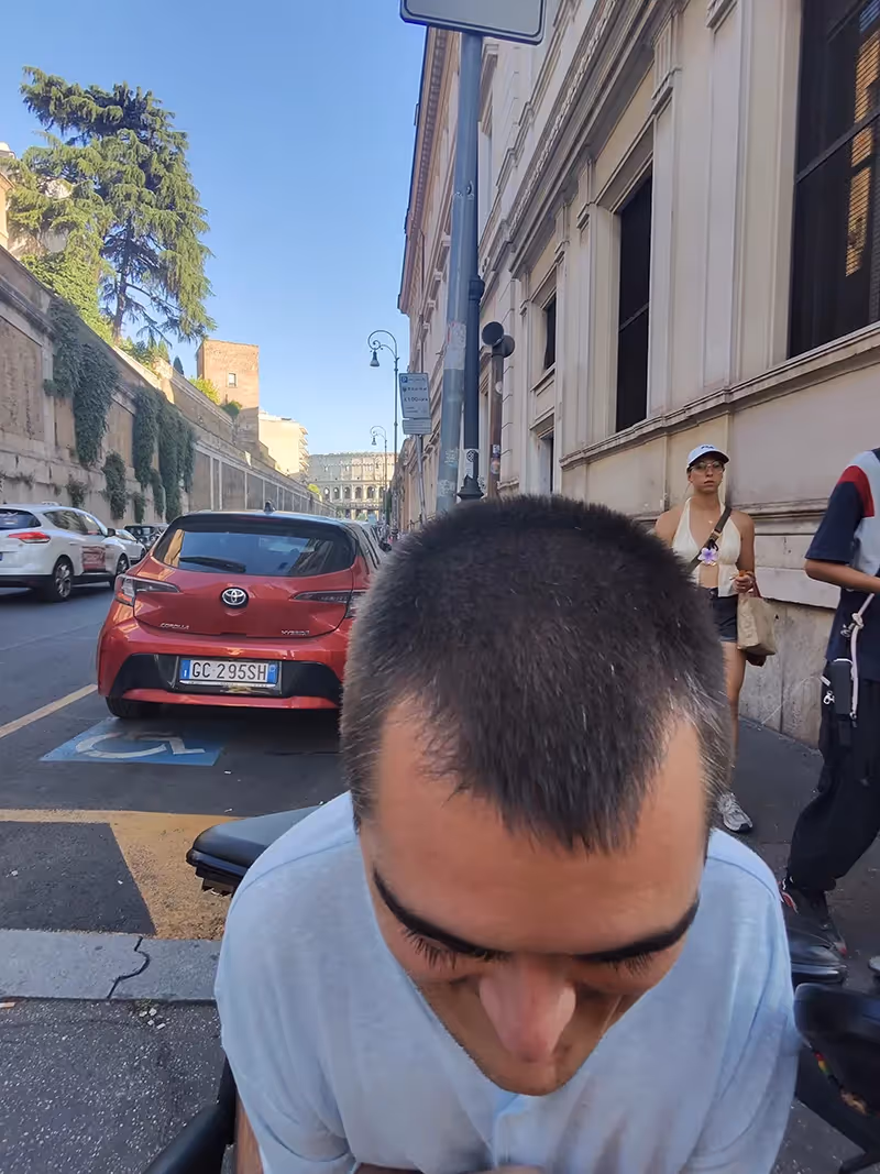 A man leaning over revealing the Roman Colosseum behind him