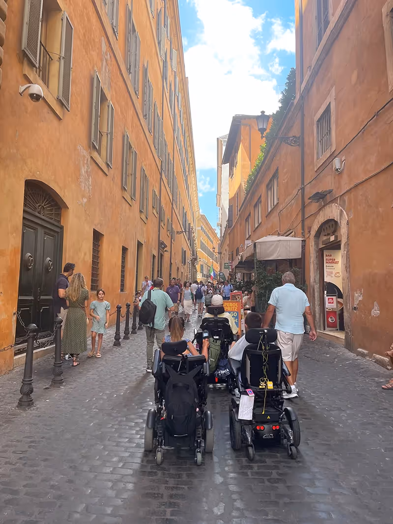 Three people in wheelchairs driving on cobblestones through an Italian street