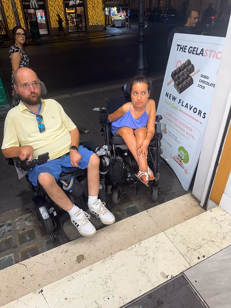 Two people in wheelchairs with sad faces sitting at the bottom of steps