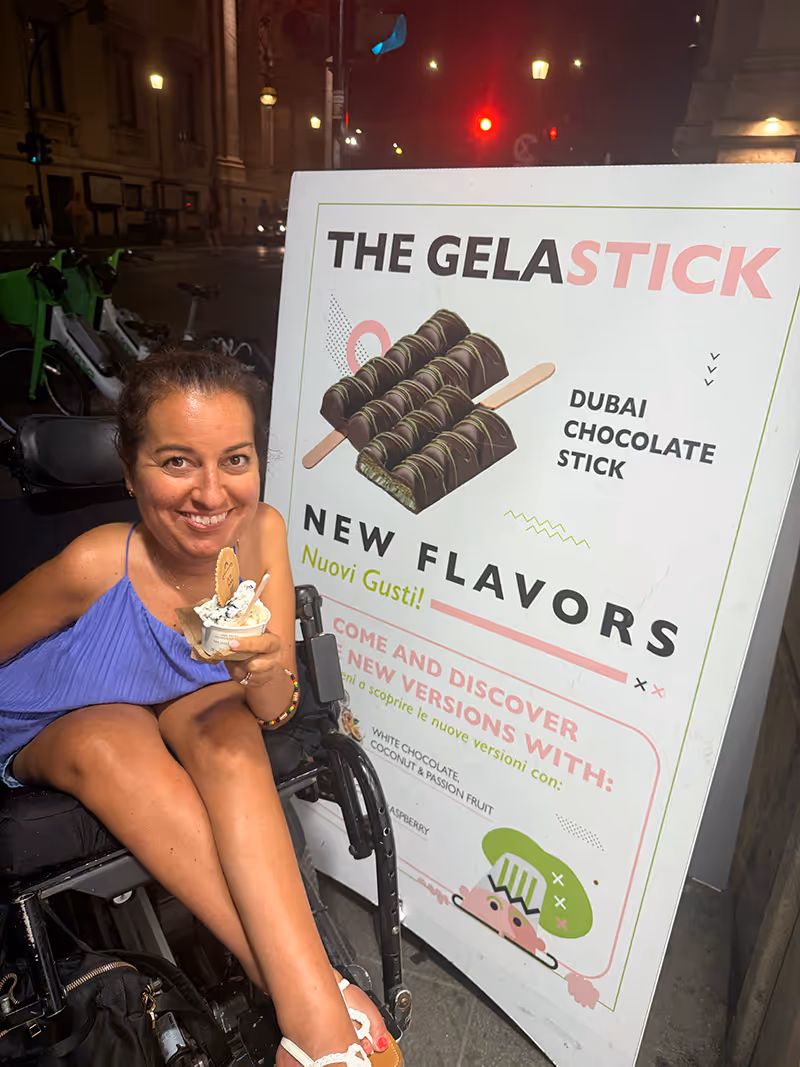 A woman with a purple tank top holding a cup of gelato smiling