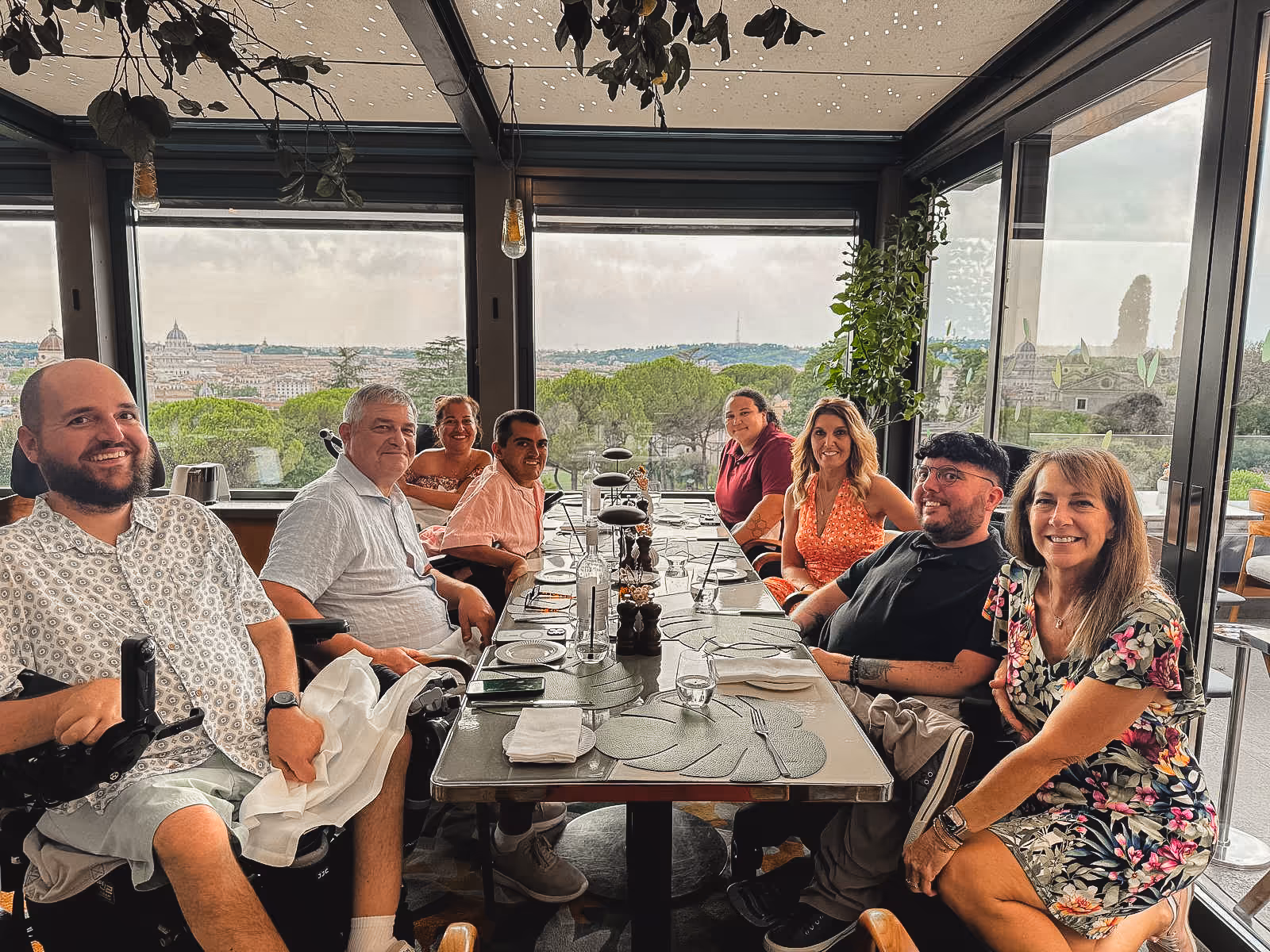 A group of people at a dinner table smiling with a sky high view of Rome in the background