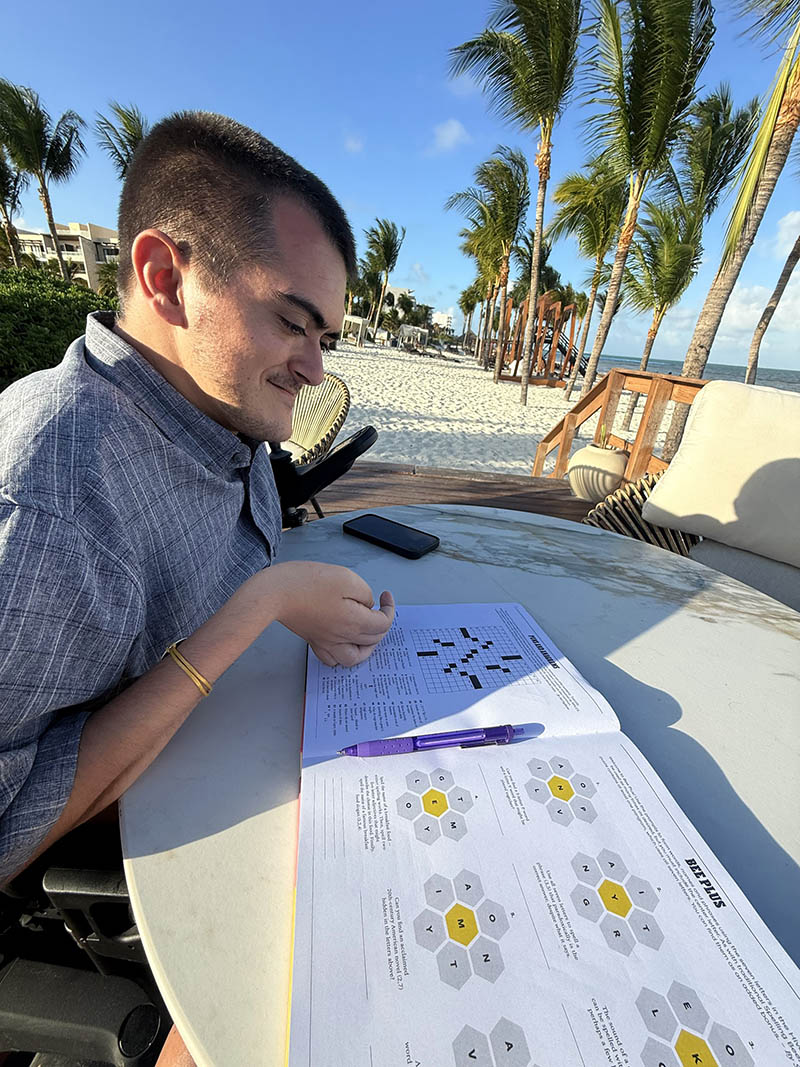 Man looking at crossword puzzle book with palm trees in the background