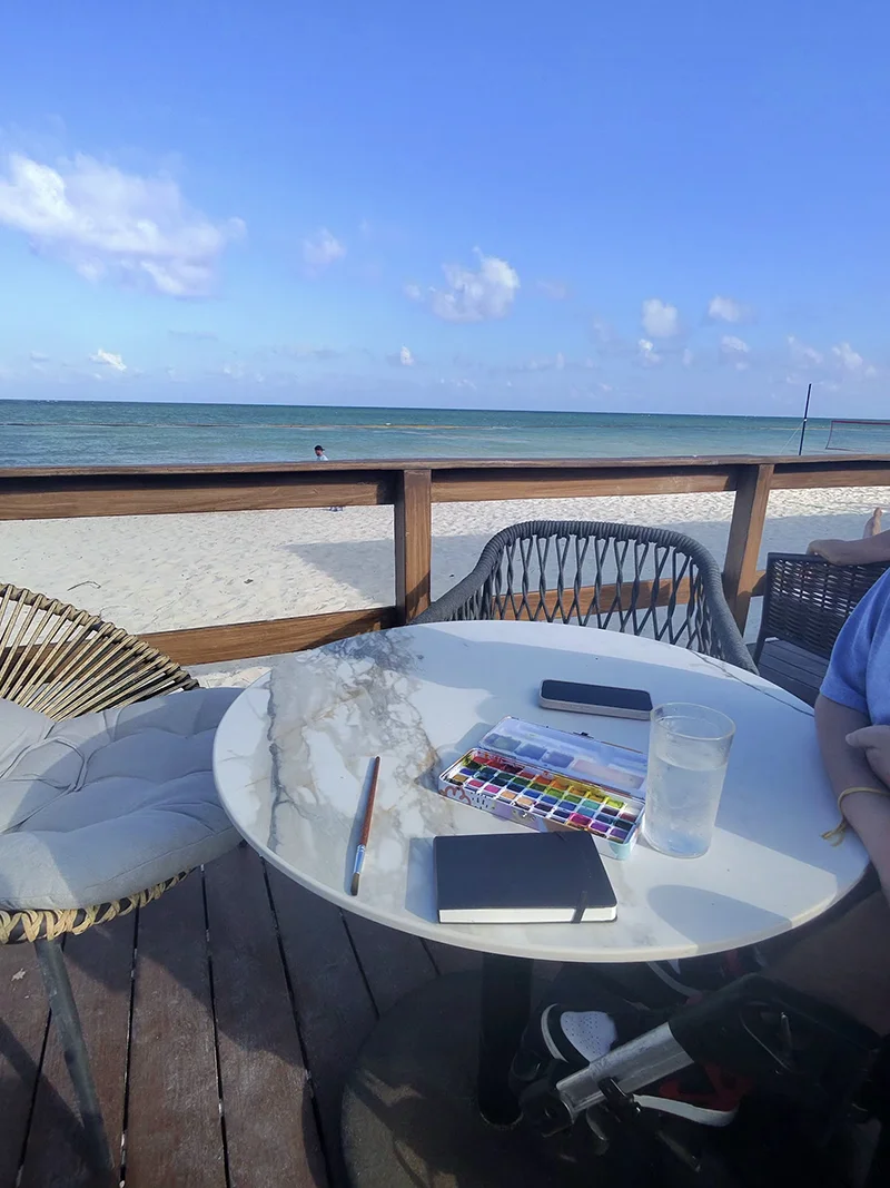 Watercolor paint on a table with the ocean in the background