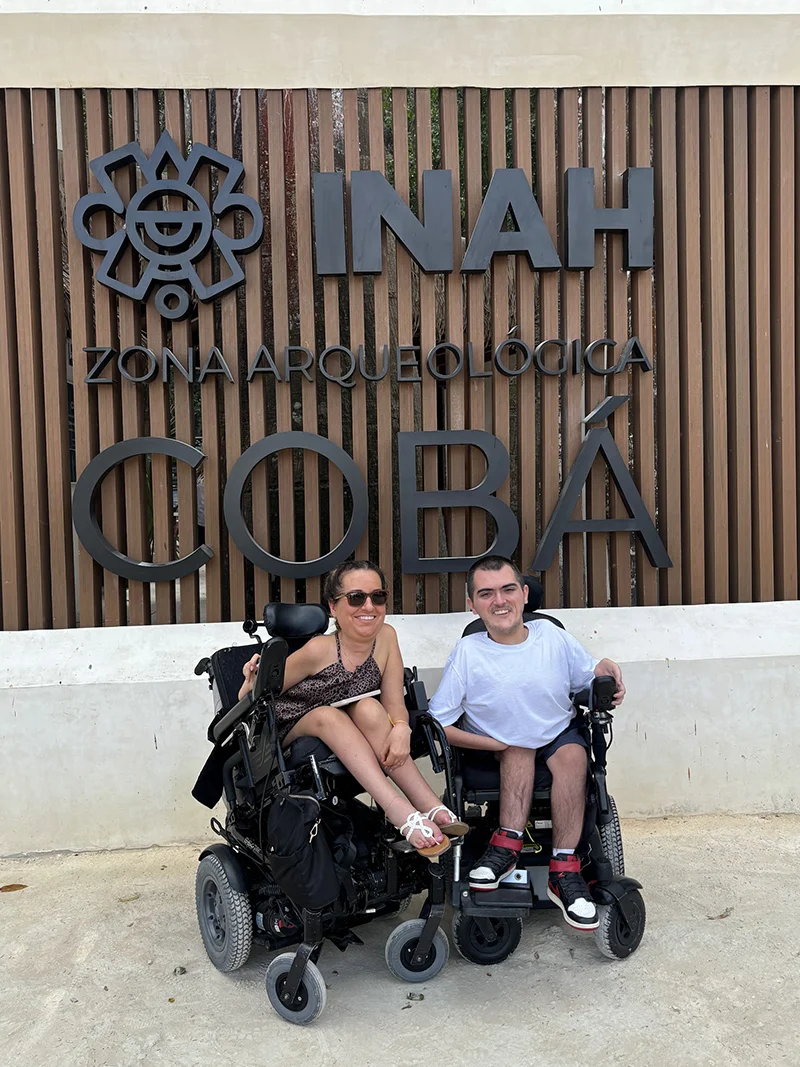 Travelers in wheelchairs at the entrance sign for Coba ruins