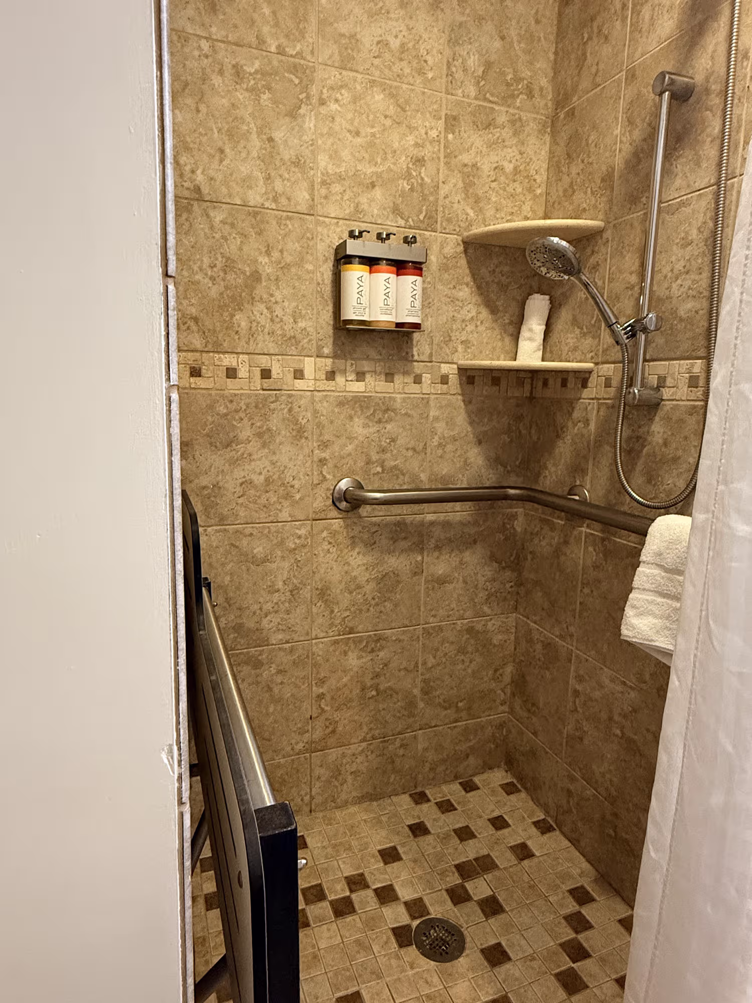 Small roll-in shower at Shephard’s Beach Resort with grab bars, handheld shower head, and built-in seat