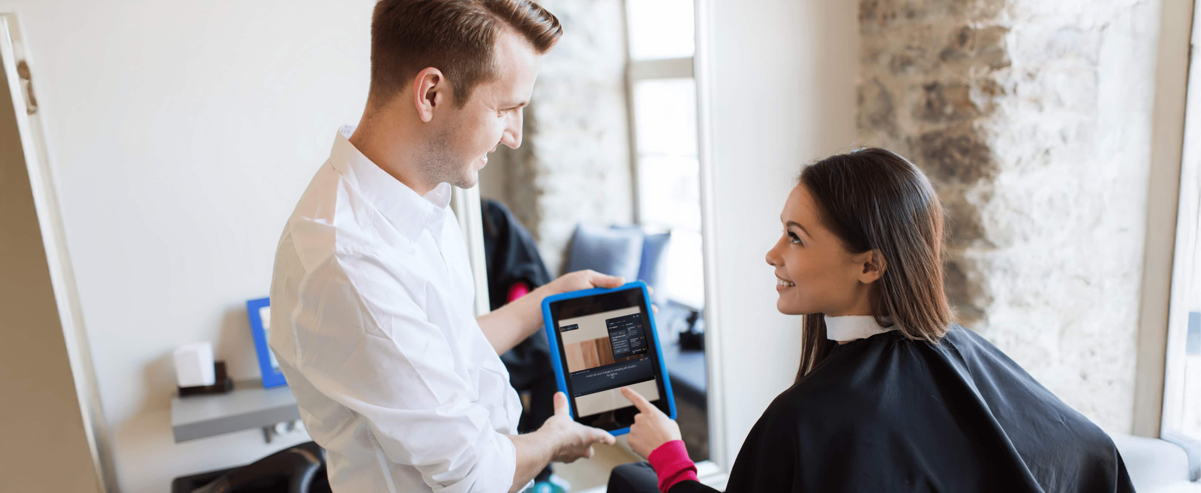 A hairstylist shows a tablet in which modus app is listening conversion to a smiling woman seated in a salon chair with a black cape.