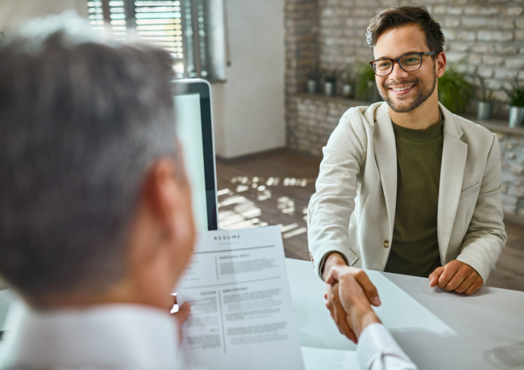 Smiling man in glasses shaking hands with interviewer holding a resume during a job interview.