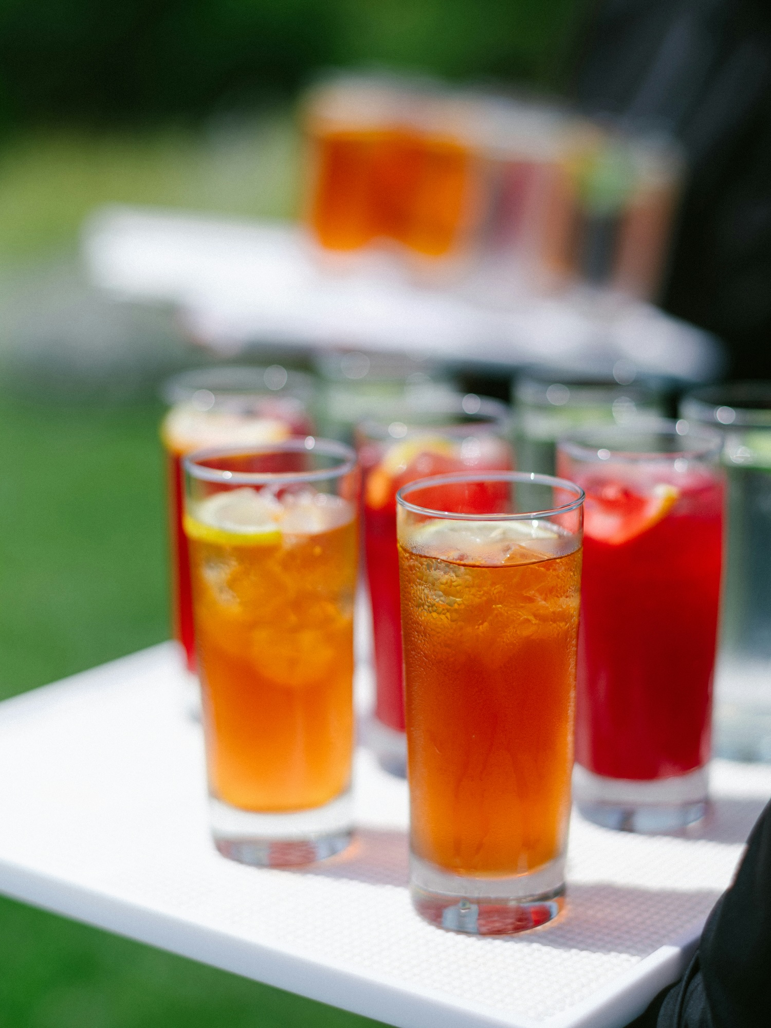 Tray of iced tea and red fruit drinks garnished with lemon slices outdoors.