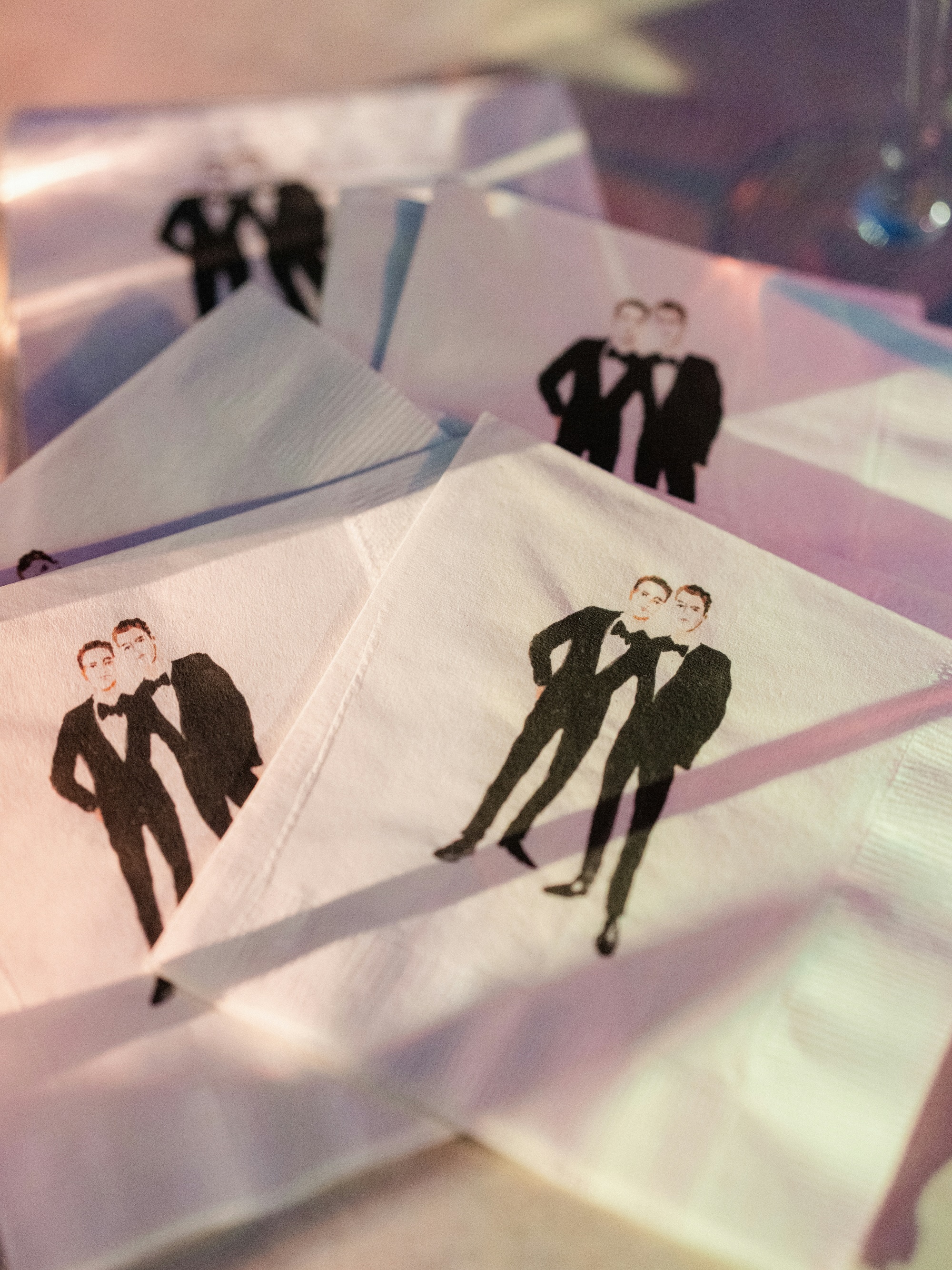 White napkins printed with an illustration of two men in tuxedos standing together.