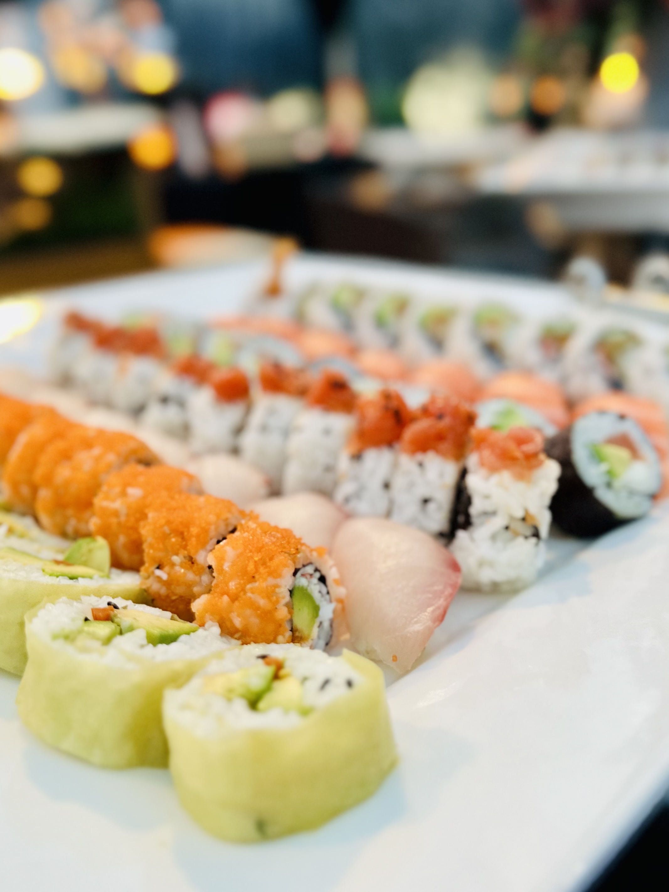 Assorted sushi rolls arranged in rows on a white plate with a variety of toppings and fillings.