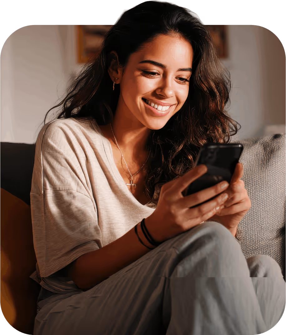 Mujer sonriente usando un teléfono móvil mientras está sentada en un sofá.