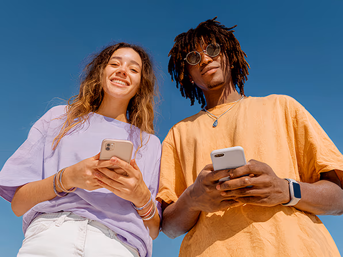 Hombre sonriente usando un teléfono móvil mientras está sentado en un sofá en una sala con estanterías de libros.