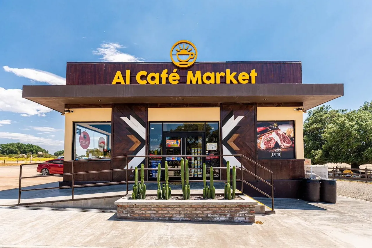 Fachada de Al Café Market con plantas de cactus frente a la entrada y un cielo azul despejado.